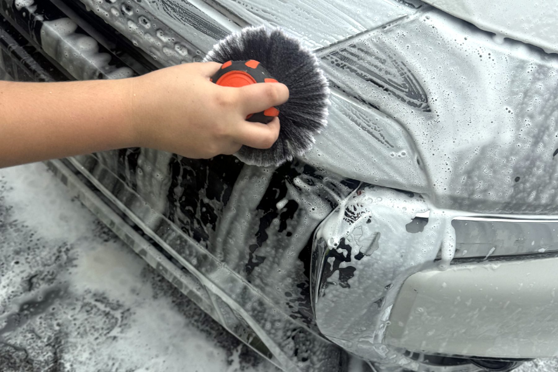 Detail brush scrubbing soapy suds off a chrome front grille — mobile car wash Wilmington NC